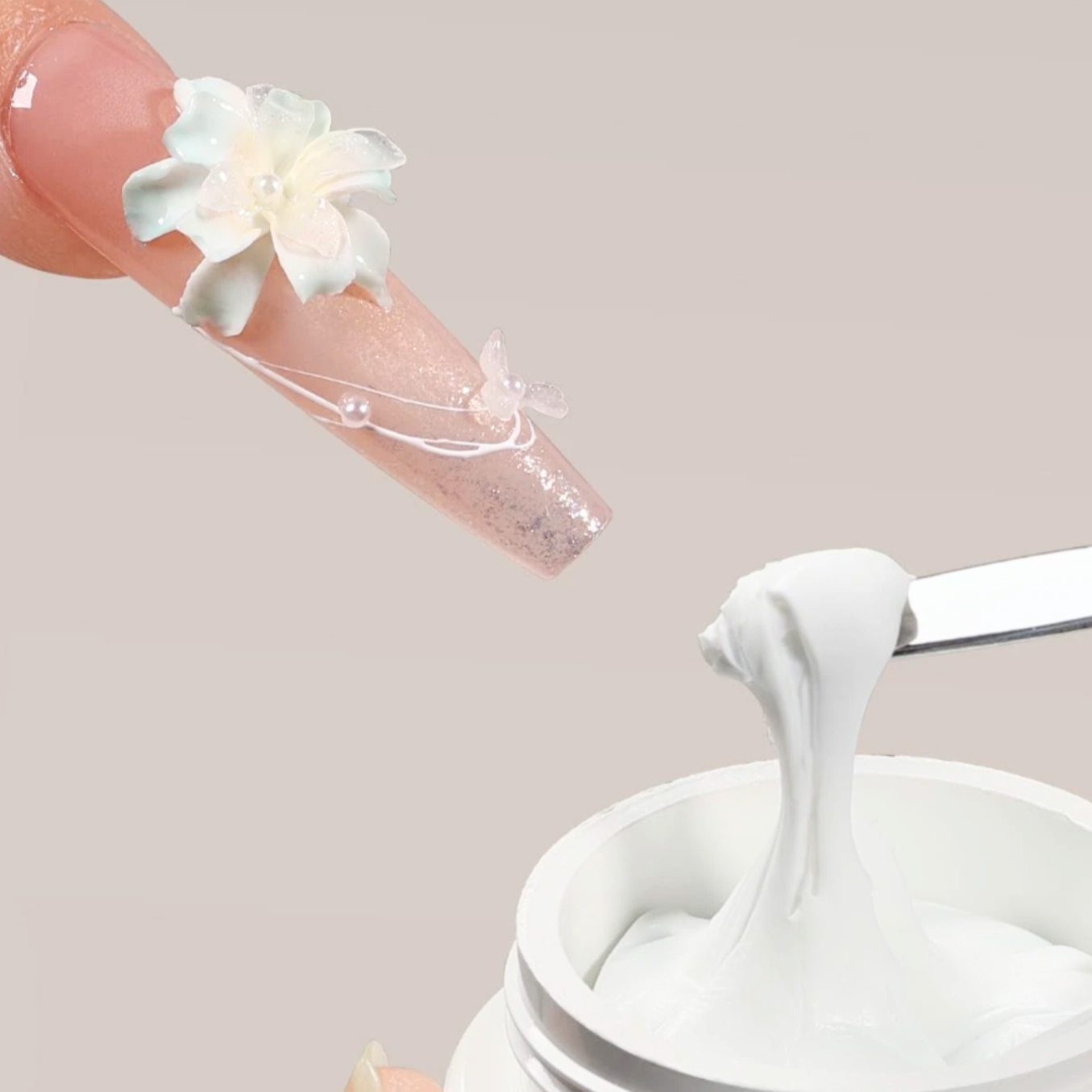 Close-up of a hand with a decorative nail design holding a small white flower above a container of white cream.