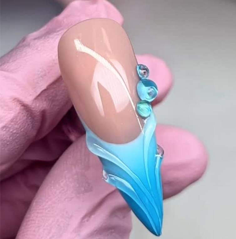 Nail art with blue wave design and small beads on a pink background